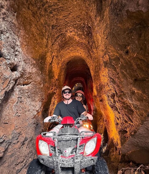 Two people in helmets on a red ATV in a rocky tunnel. 2