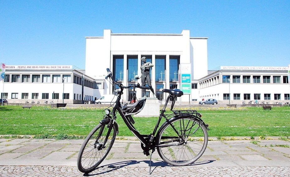 A bicycle parked in front of a modern building with large windows and a grassy area. 1