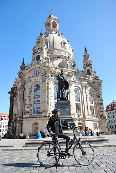 A person on a bicycle in front of a historic building with a statue. 2