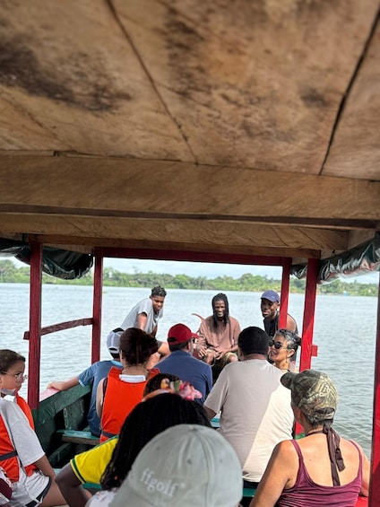 A group of people on a boat with a wooden canopy, surrounded by water and greenery. 1