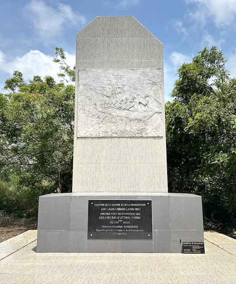 A monument with an engraved relief depicting a historical scene, surrounded by trees. 3