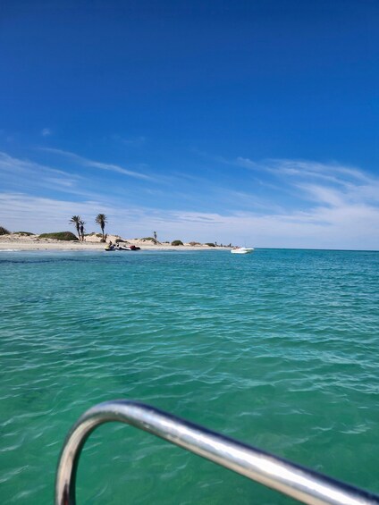 A clear turquoise sea, a sandy beach with palm trees, and a distant boat. 3