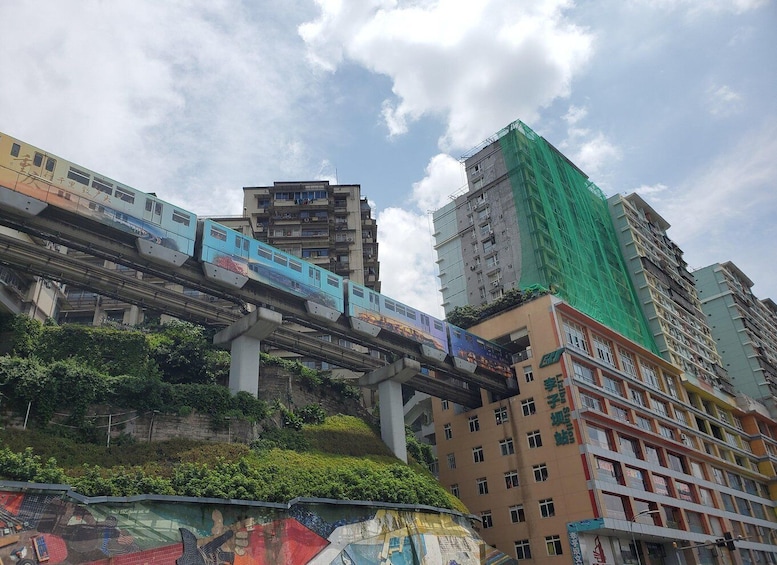 A blue train on an elevated track above a cityscape with buildings and greenery. 3