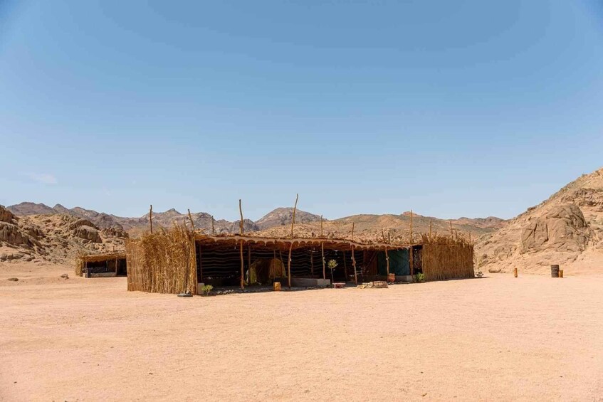A desert landscape with a thatched-roof structure and mountains in the background. 3