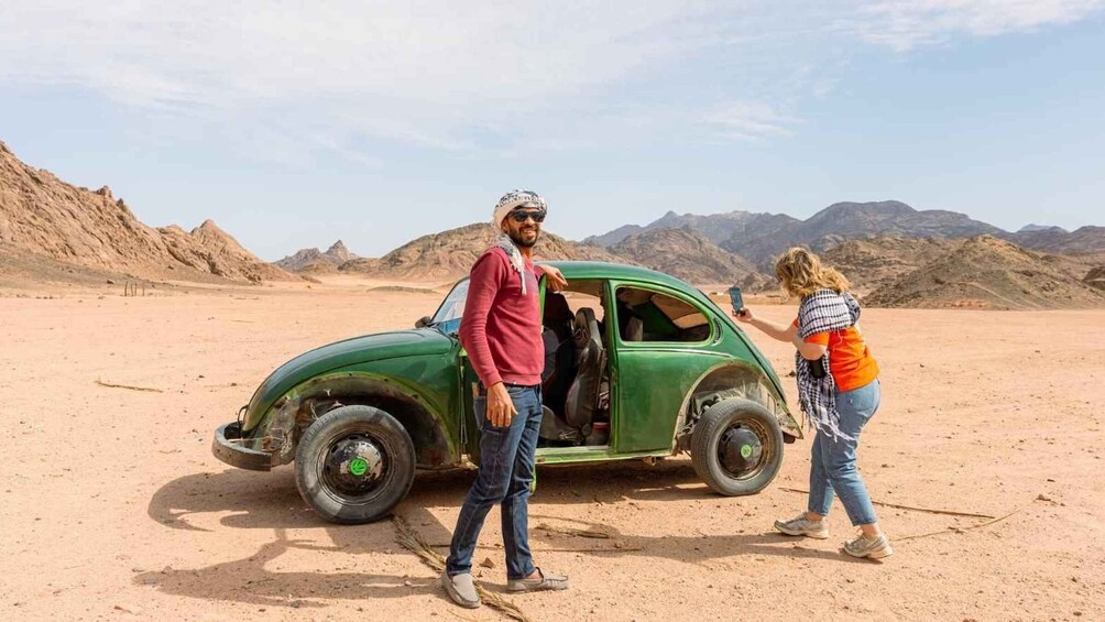 A green vintage car in a desert with mountains in the background. 4