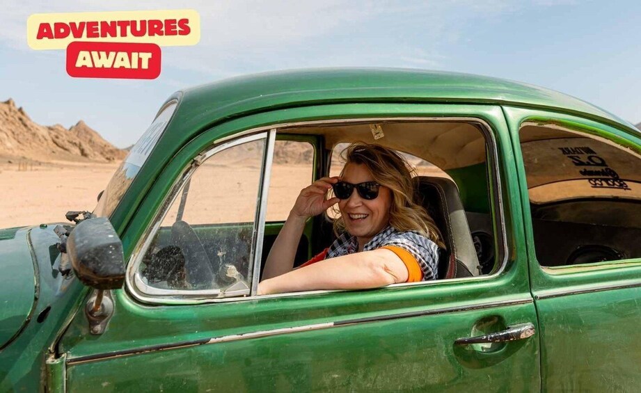 A person in a green vintage car with a desert landscape in the background. 1