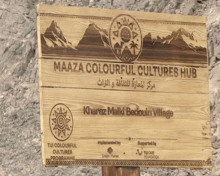 A wooden sign with 'MAAZA COLOURFUL CULTURES HUB' and 'Kharaz Malki Bedouin Village' text, along with logos for TUI COLOURFUL CULTURES PROGRAMME, Green Planet, and TUI CARE FOUNDATION. 2