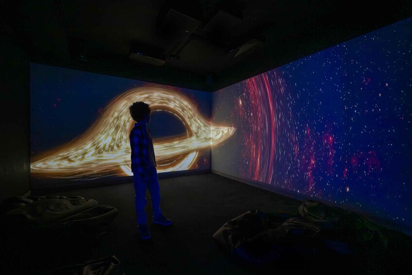 A person standing in a room with a large, illuminated space-themed mural on the wall. 1