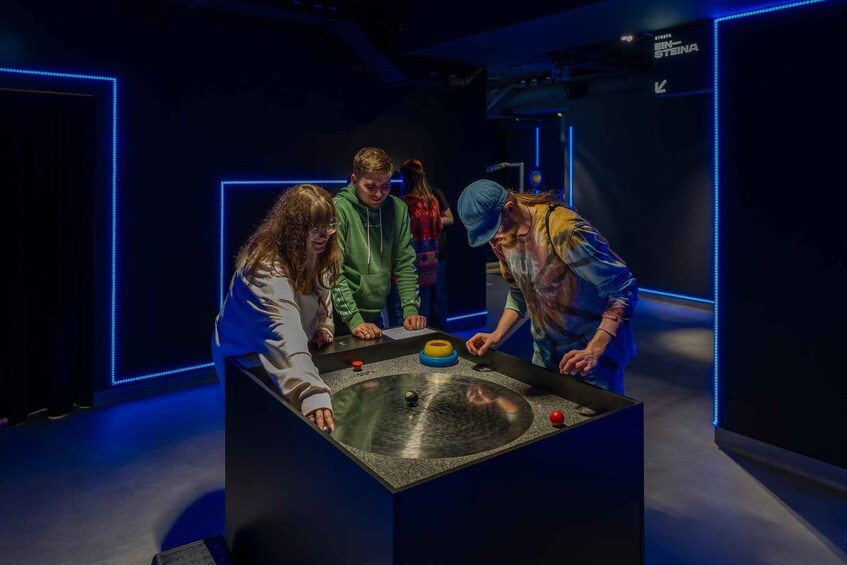 A group of people interacting with a table in a dimly lit room with blue neon lighting. 4