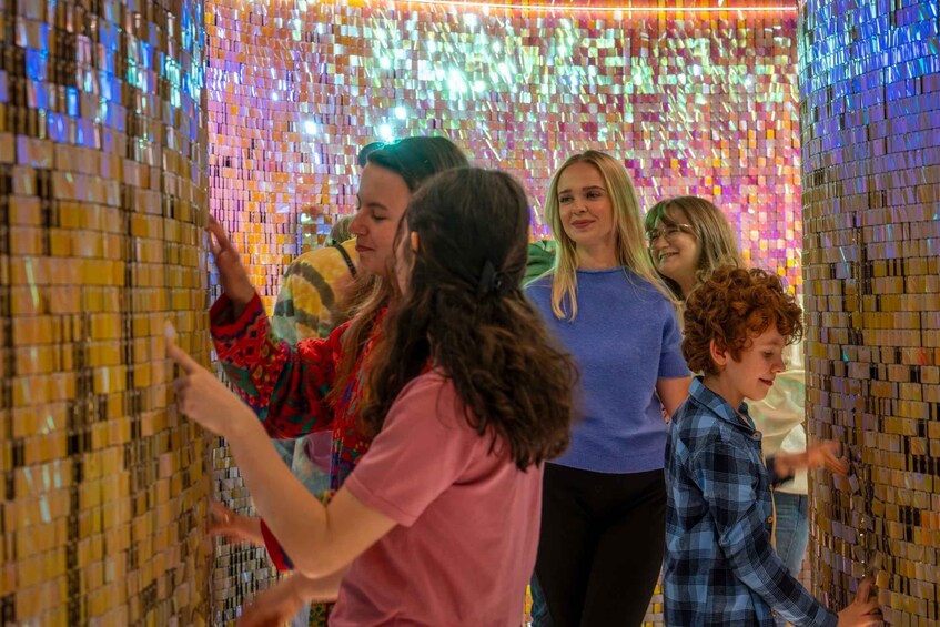 A group of people interacting with a wall of colorful, reflective tiles. 3