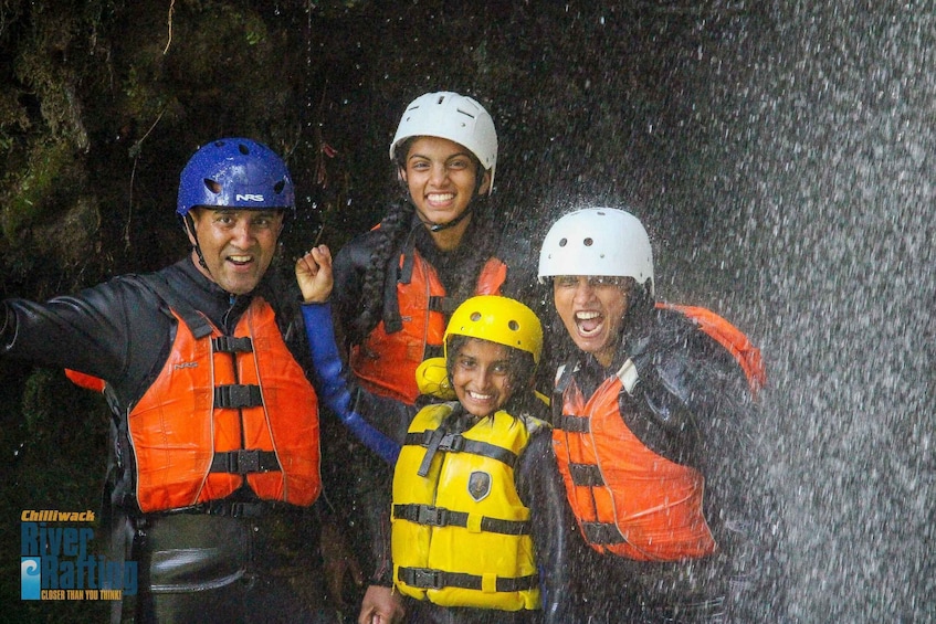 Four people wearing helmets and life vests, with water splashing around them. 2