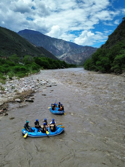 A river with two blue inflatable rafts, surrounded by mountains and greenery. 4