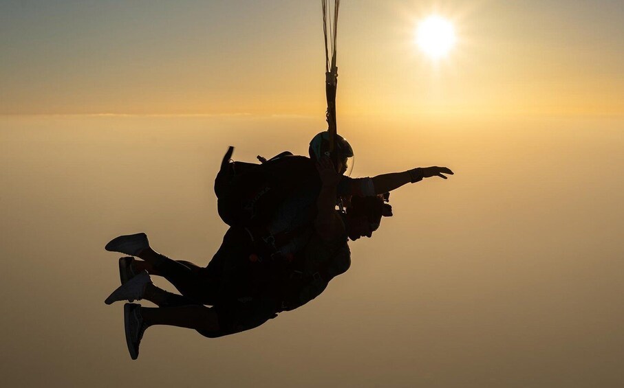 A person in freefall with a parachute, against a sunset sky. 5