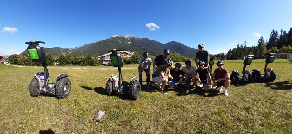 A group of people with Segways in a grassy field with mountains in the background. 1