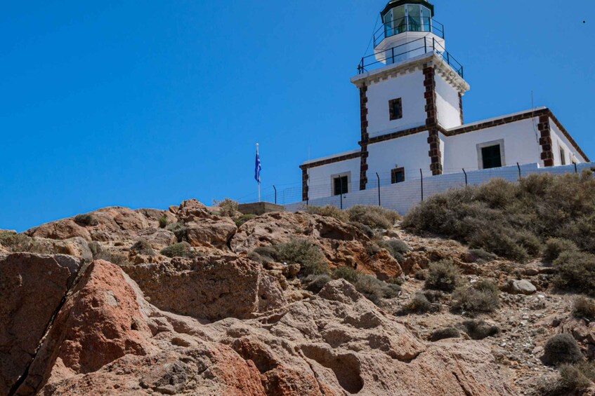 A white lighthouse with a green top, situated on a rocky hill with sparse vegetation. 3