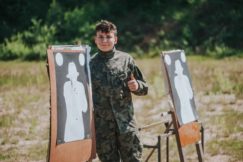 A person in military camouflage standing next to two target boards with silhouettes. 3