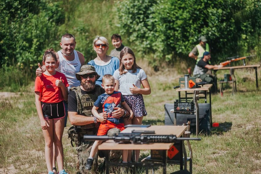 A group of people in an outdoor setting with a table and a rifle in the foreground. 2