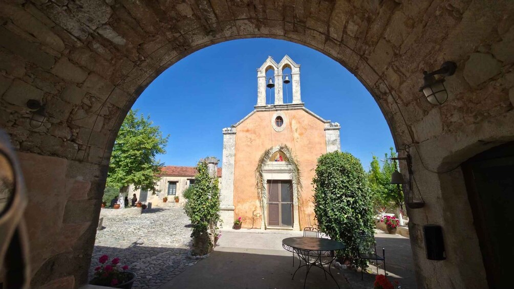 An archway framing a church with a bell tower, surrounded by cobblestone paths and potted plants. 1