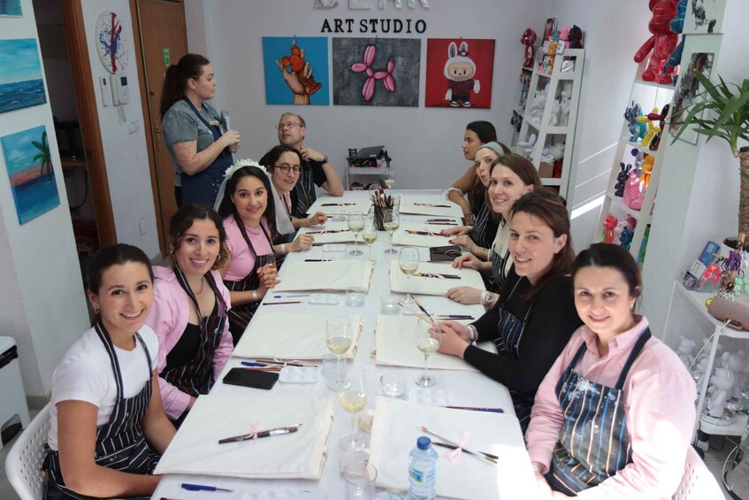 A group of people seated around a table in an art studio, engaged in painting activities. 2