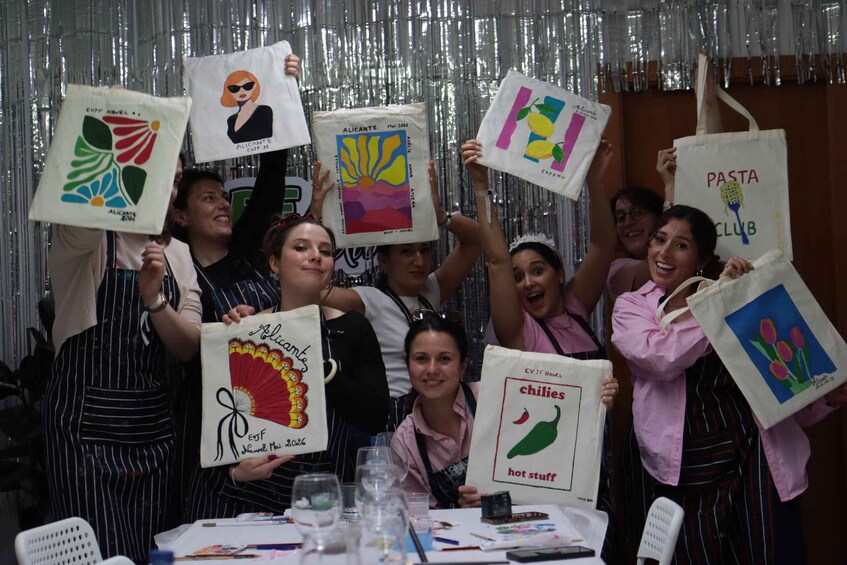A group of people holding up painted tote bags with various designs. 3