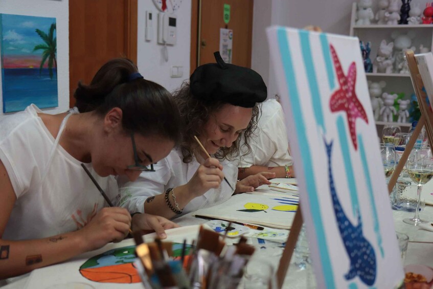 Two people painting at a table with art supplies and a painting in progress. 2