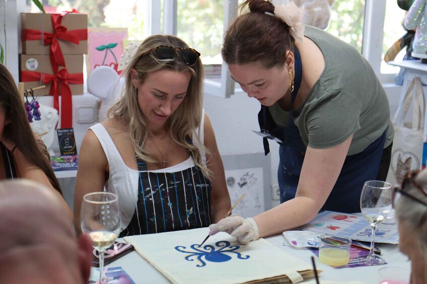 Two people painting on a canvas at a table with art supplies and a wine glass. 4