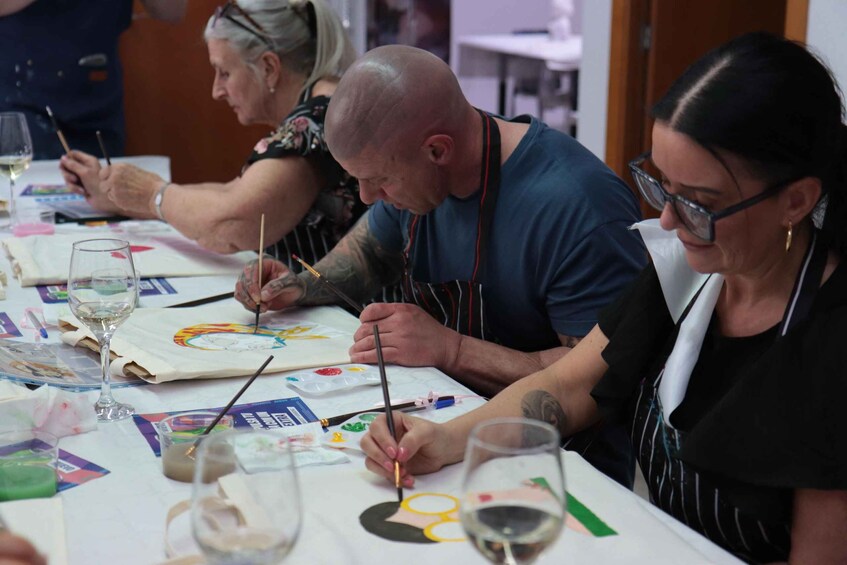 People painting on canvases at a table with wine glasses. 5