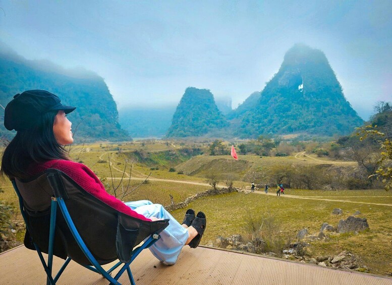 A person seated in a chair overlooking a mountainous landscape with a dirt path and a red flag. 4