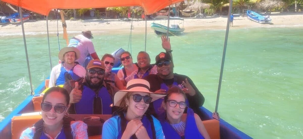A group of people on a boat near a beach with clear water and a boat docked on the shore. 2