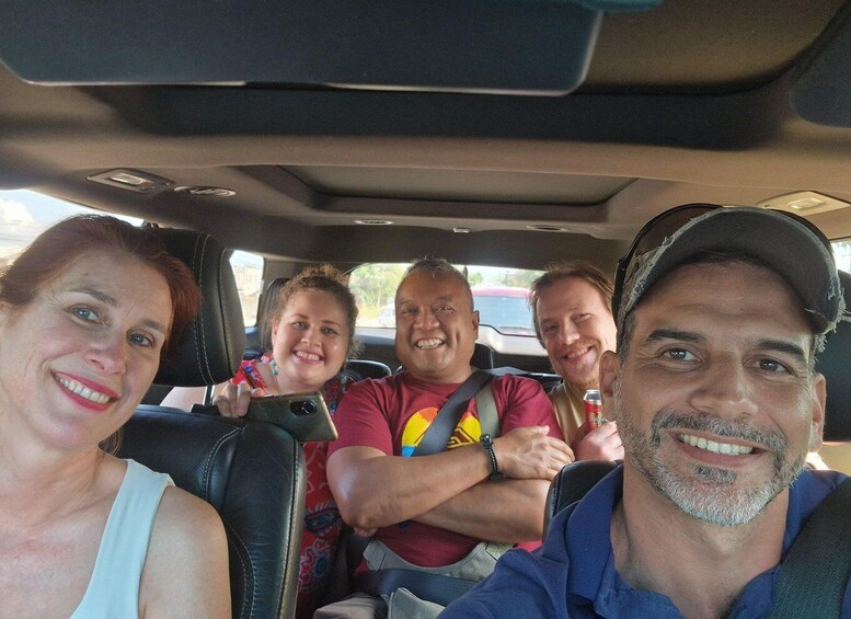 Four people seated in a car with a sunroof, windows, and a steering wheel. 5