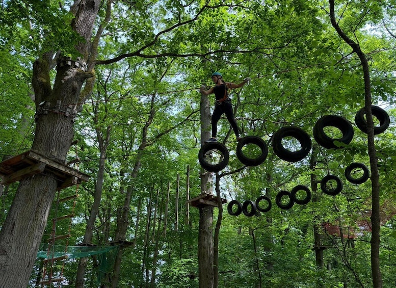 A person navigating a forest obstacle course with tire rings and wooden platforms. 1