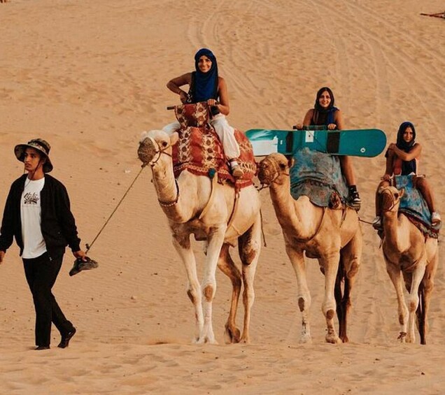 A person leading camels with riders in traditional attire. 1