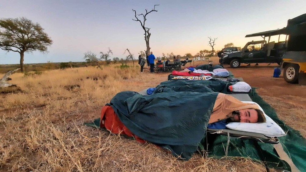 A campsite with tents and a vehicle in a dry grassland area with sparse trees. 1