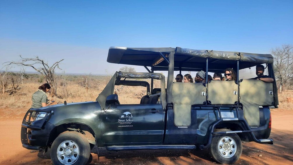 A safari vehicle with passengers, a guide, and a dry, open landscape with sparse vegetation. 4