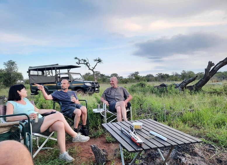 Three people sitting on chairs outdoors with a vehicle and a picnic table in the background. 5