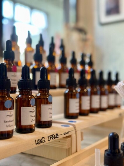 A row of amber bottles with droppers, labeled with various scents like vanilla and sandalwood, on a wooden shelf. 4
