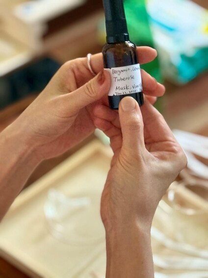 A person holding a small bottle labeled 'Bergamot Extract, Tubercleose Mask, Varnish.' 1