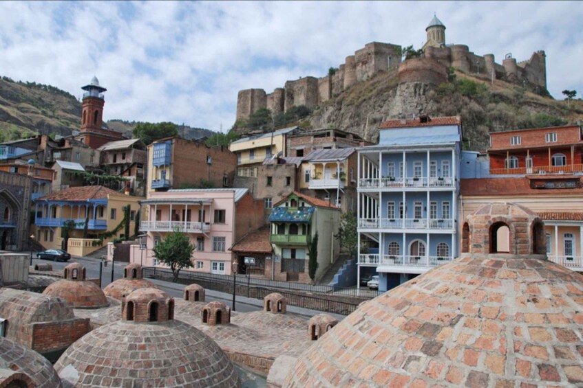 A historic town with colorful buildings, domed structures, and a large fortress on a hill. 1