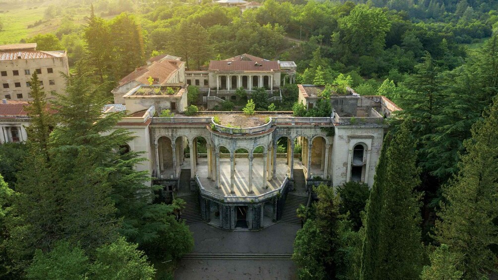 A grand, historic building with arched walkways and a central dome, surrounded by lush greenery. 2
