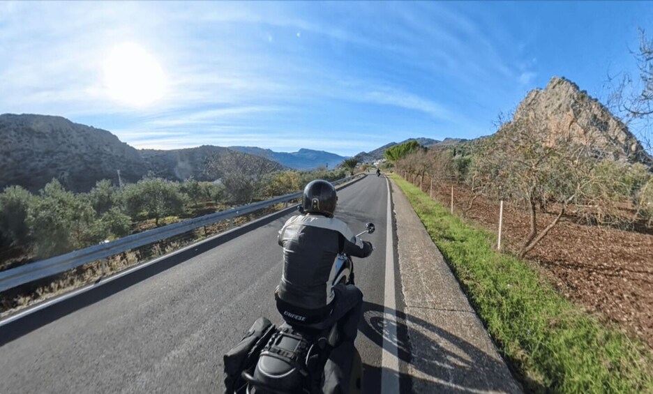 Un motociclista conduce por una carretera con montañas al fondo. 1