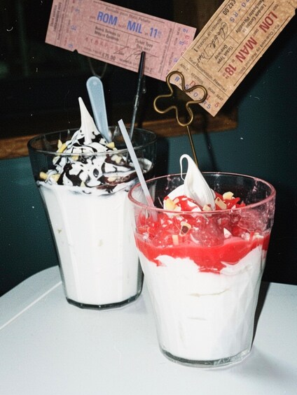 Two dessert cups with toppings, one with chocolate and the other with red sauce, on a table with a ticket and a keychain in the background. 3