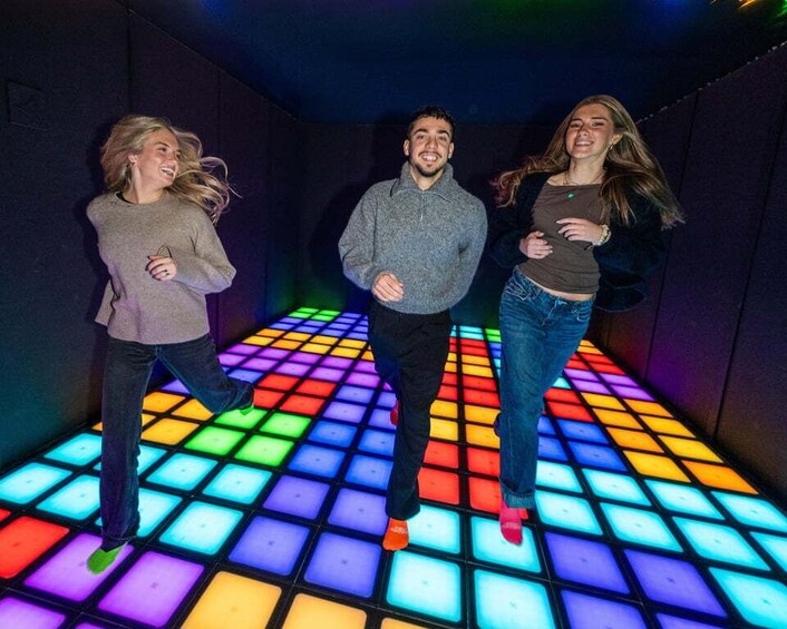 Three people dancing on a floor with colorful square tiles. 3
