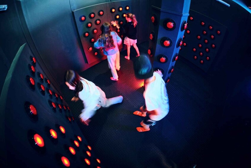 A group of people interacting with a wall of illuminated buttons. 1