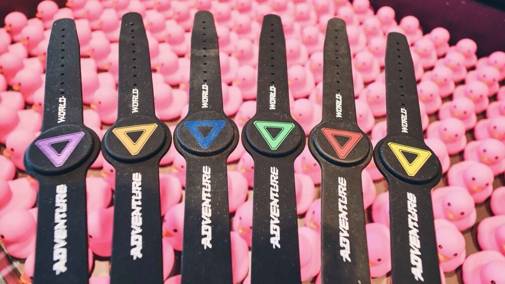 A row of black Adventure-themed keychains with colorful triangle symbols, set against a background of pink rubber ducks. 5