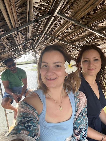 A person taking a selfie under a thatched roof structure by a body of water. 2