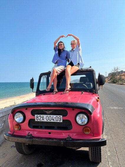 Two people making a heart shape with their hands on a red car parked by the beach. 5