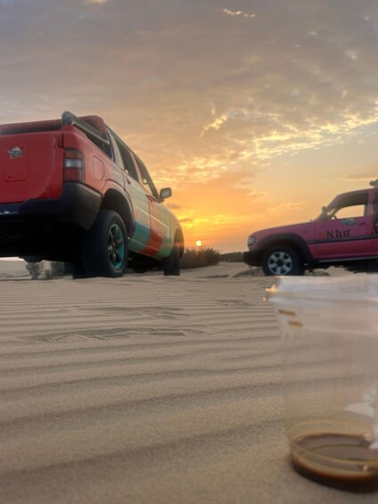 Two pickup trucks parked on a sandy surface with a sunset in the background. 4