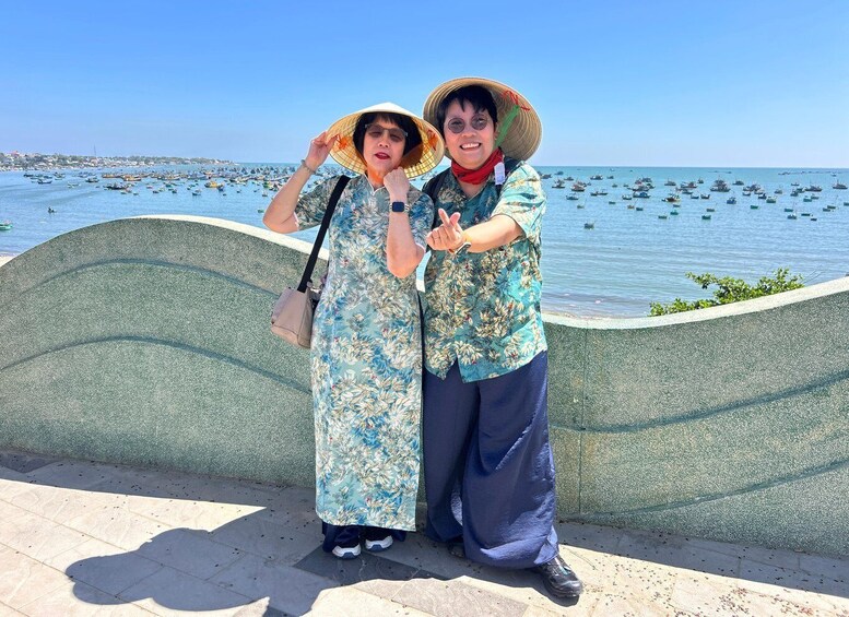 Two people standing by a waterfront with boats in the background. 2
