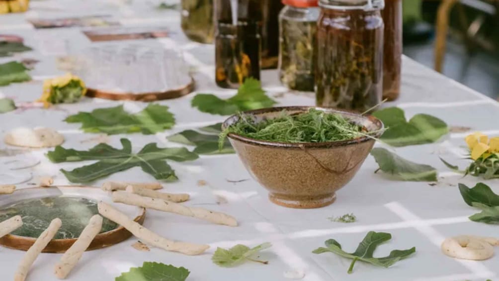 A table with a bowl of greens, scattered leaves, and some jars. 3