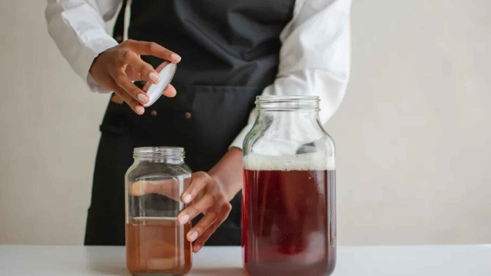 A person pouring liquid from a small jar into a larger jar. 1
